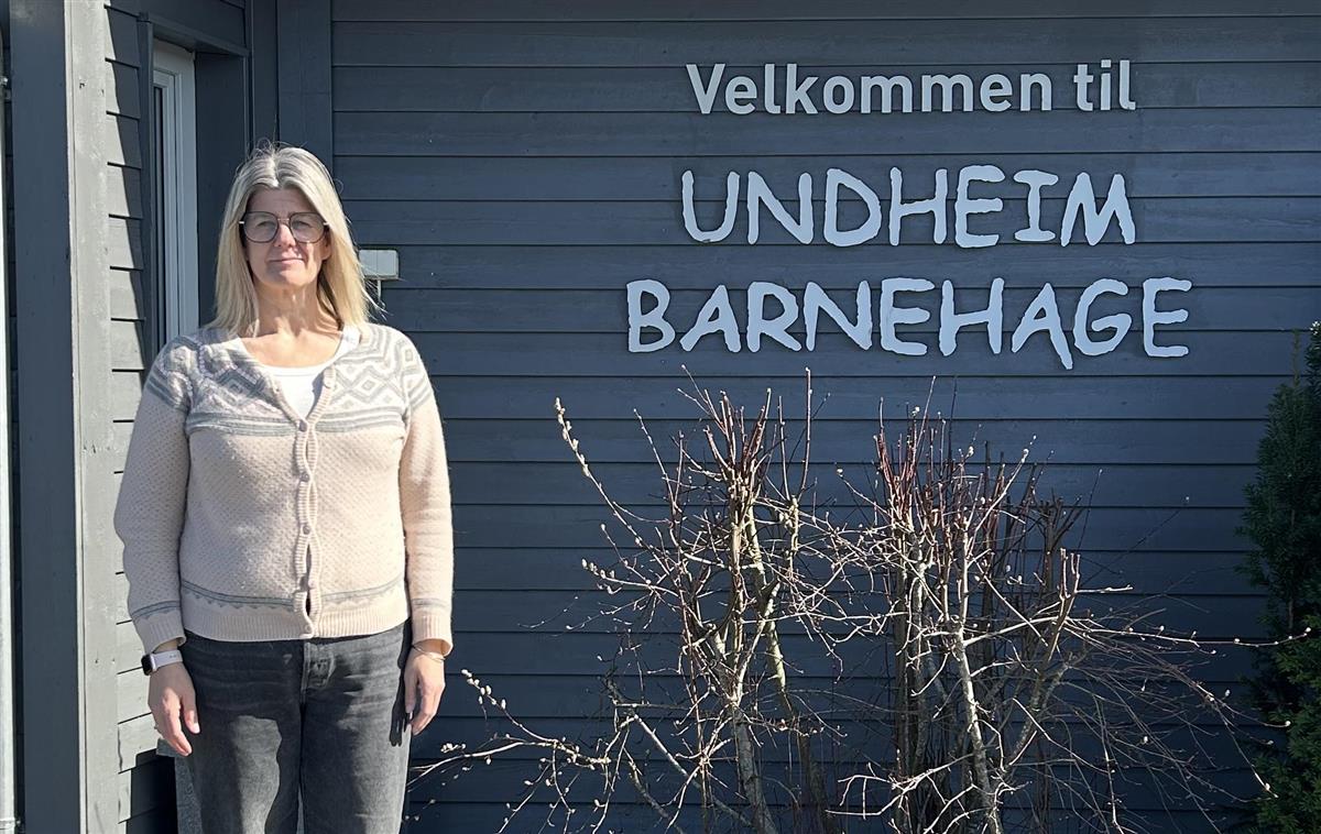 Tove Hersdal, styrar i Undheim barnehage, står foran skilt som seier "Velkommen til Undheim barnehage" - Klikk for stort bilete